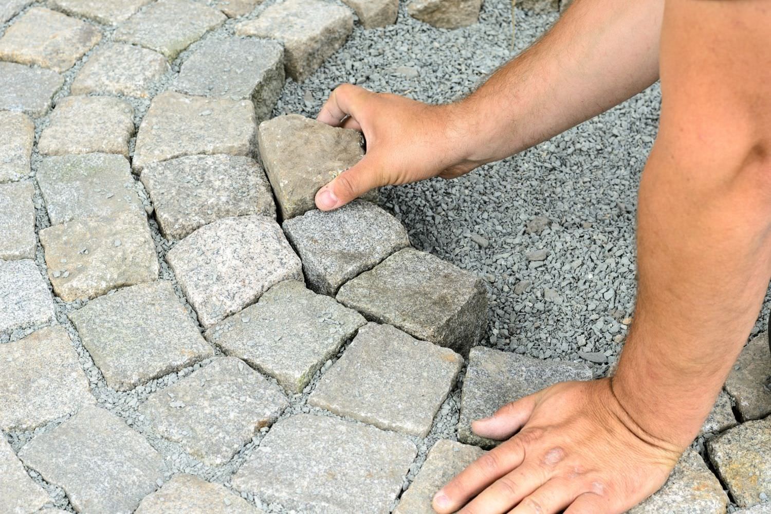 Bild zeigt: Zwei Hände eines Handwerkers verlegen Pflastersteine
