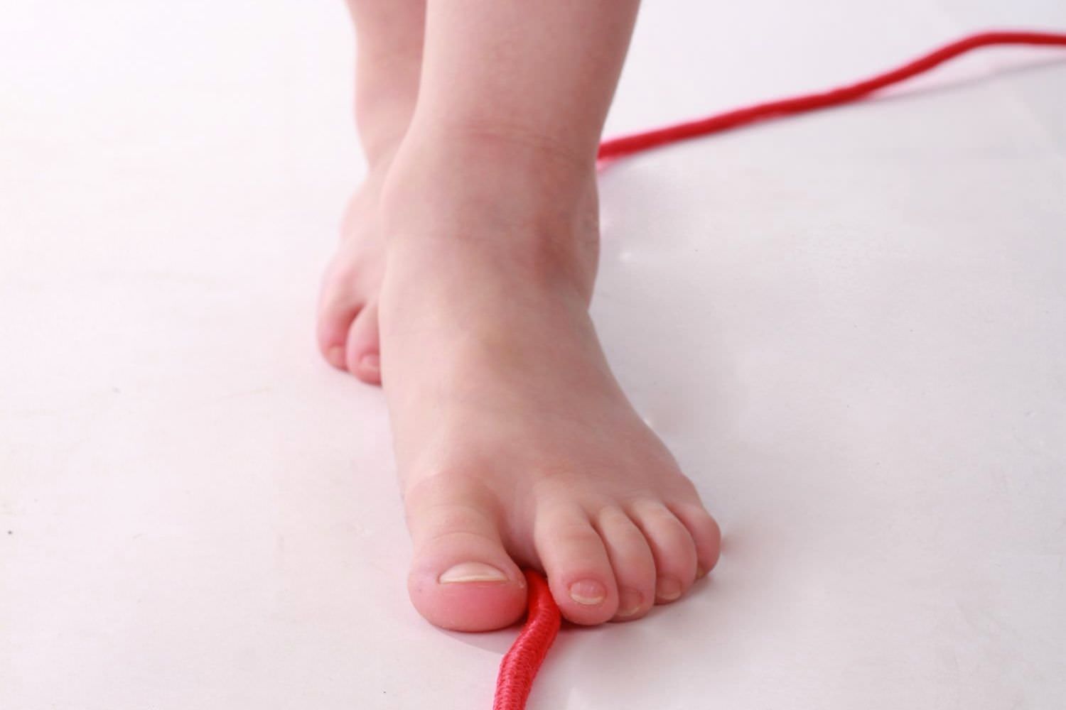Bild zeigt: Nackte Kinderfüße stehen hintereinander auf einer roten Schnur
