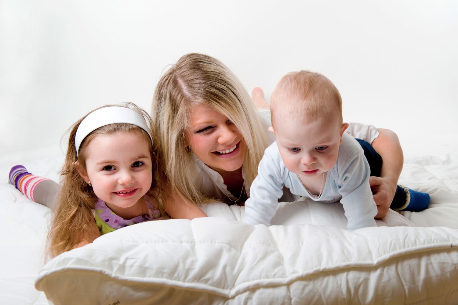 Bild zeigt: Lachende Mutter mit zwei Kindern auf der Bettdecke