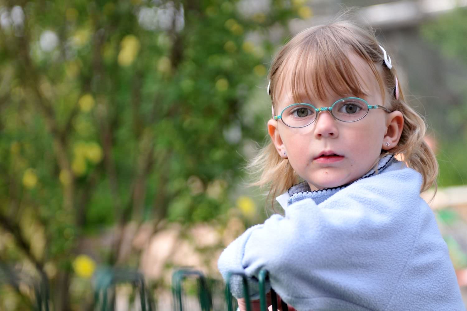 Bild zeigt: Kleines Mädchen mit Brille am Zaun