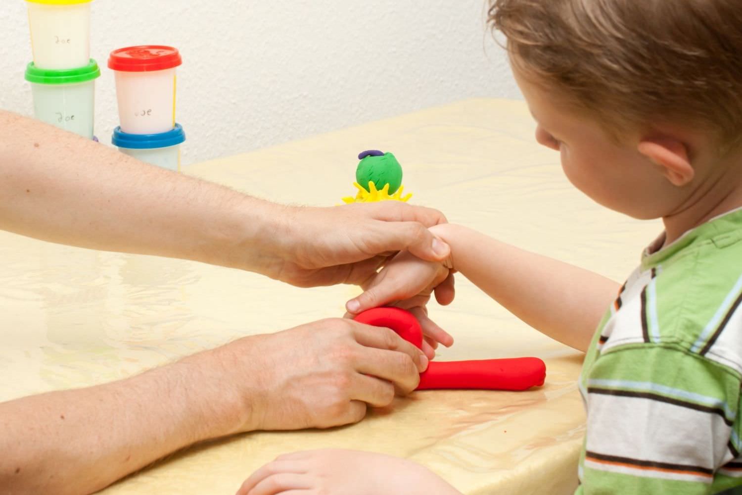Bild zeigt: Ergotherapeut erklärt einem Jungen eine Übung für die Hand mit roter Knete