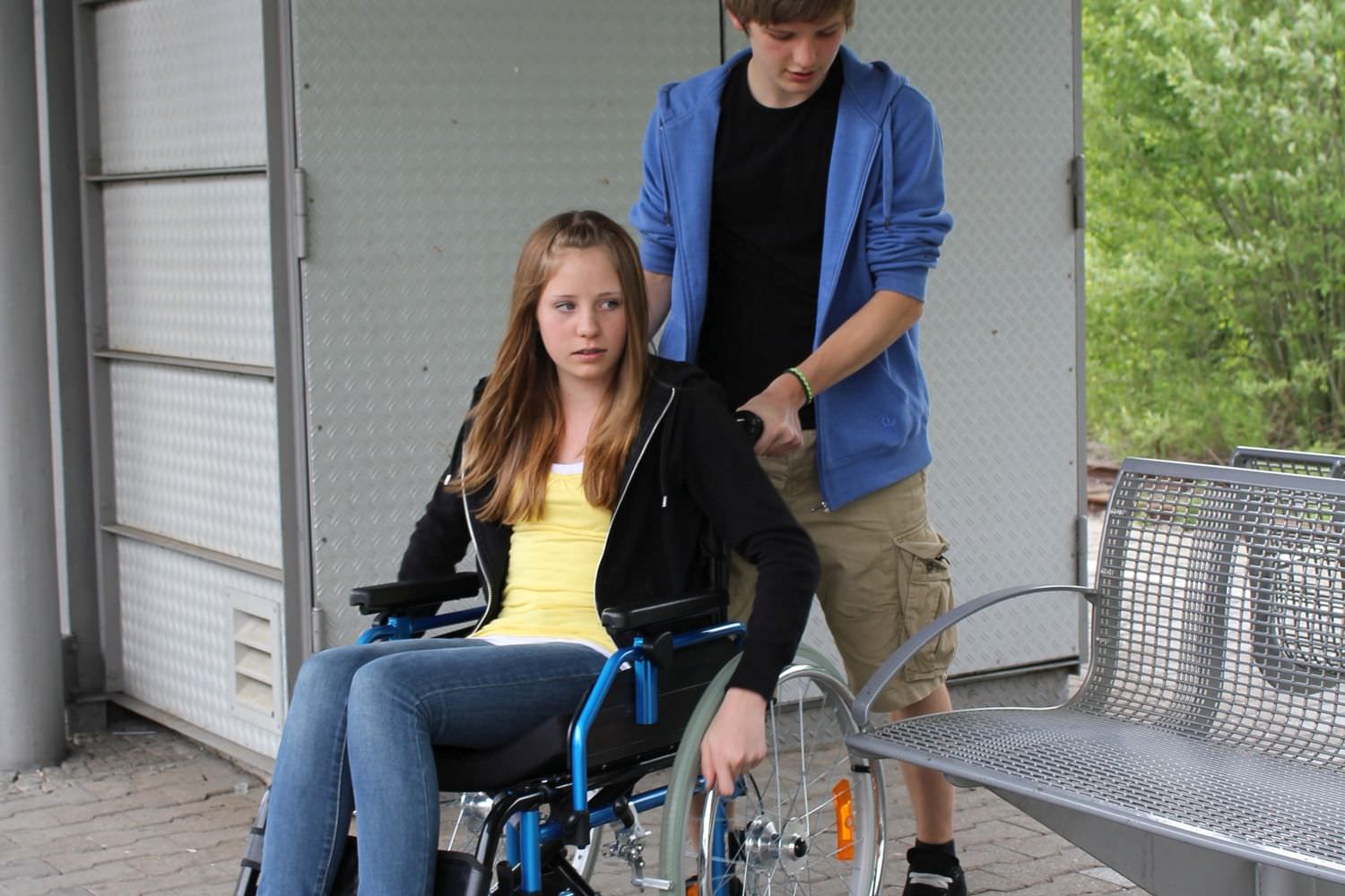 Bild zeigt: Ein Jugendlicher schiebt den Rollstuhl seiner Freundin auf einem Bahnsteig