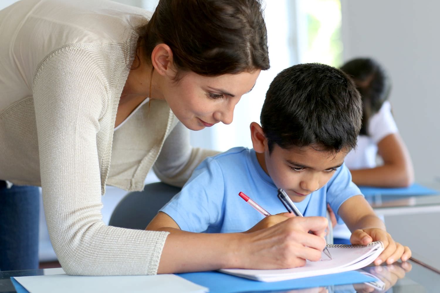 Bild zeigt: Lehrerin hilft einem Jungen beim Schreiben im Heft