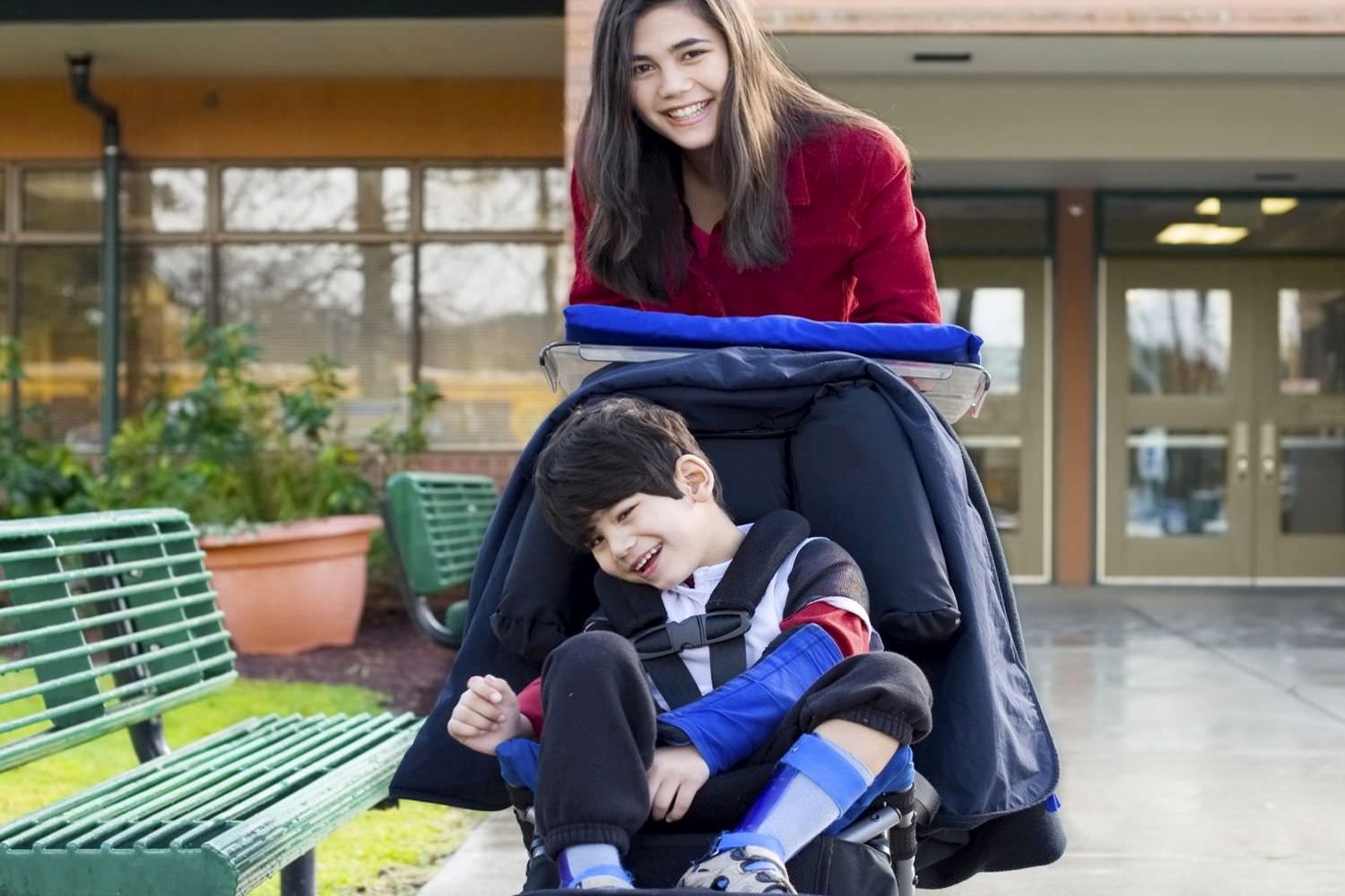Bild zeigt: Ein Junge im Rollstuhl mit seiner Integrationshelferin vor dem Schuleingang