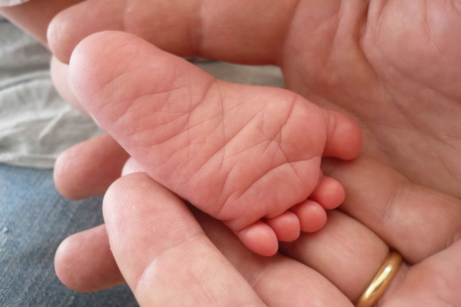 Bild zeigt: Fuß eines Säuglings in den Händen eines Erwachsenen