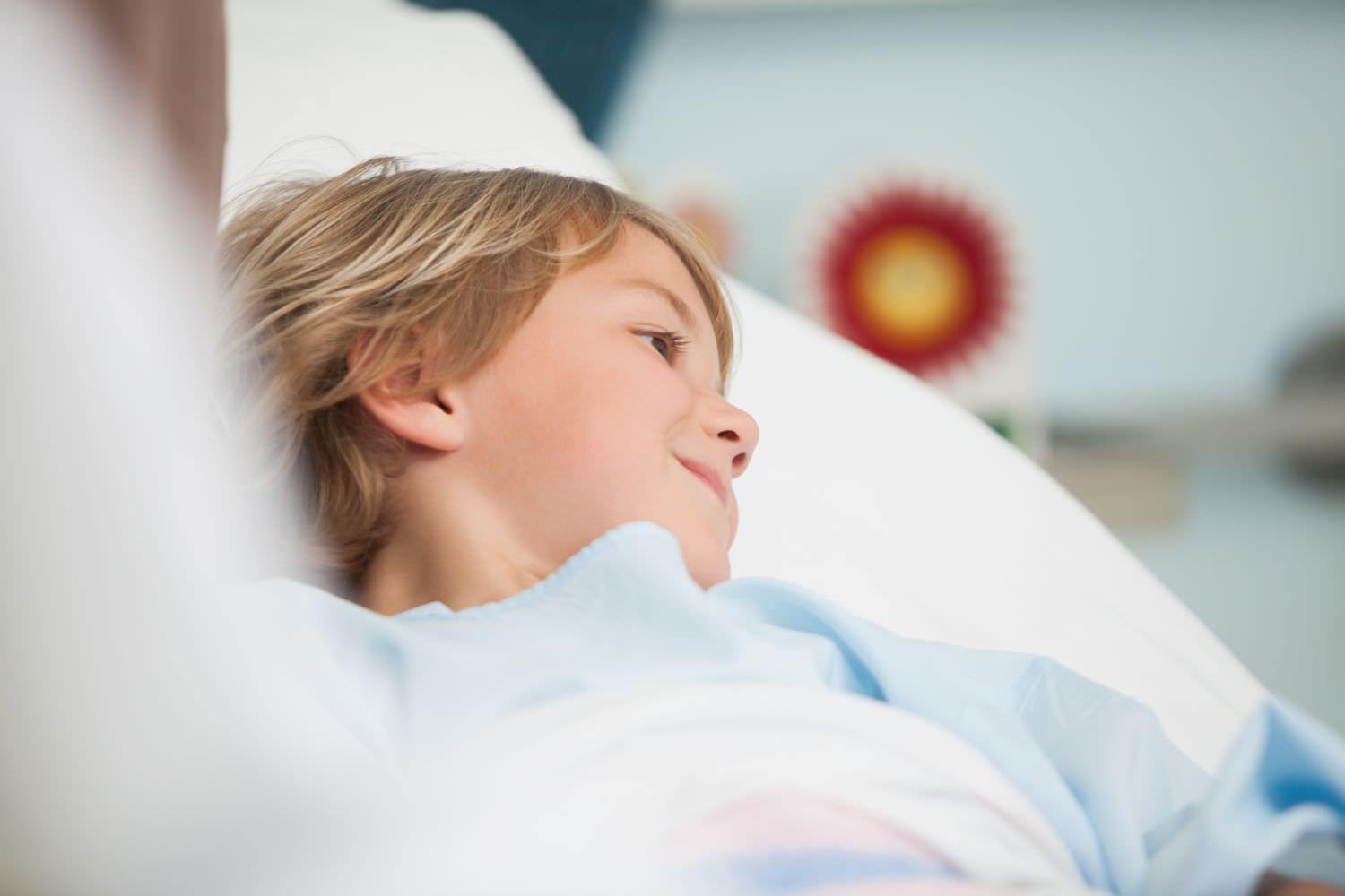 Bild zeigt: Kleiner lächelnder Junge liegt im Krankenhausbett
