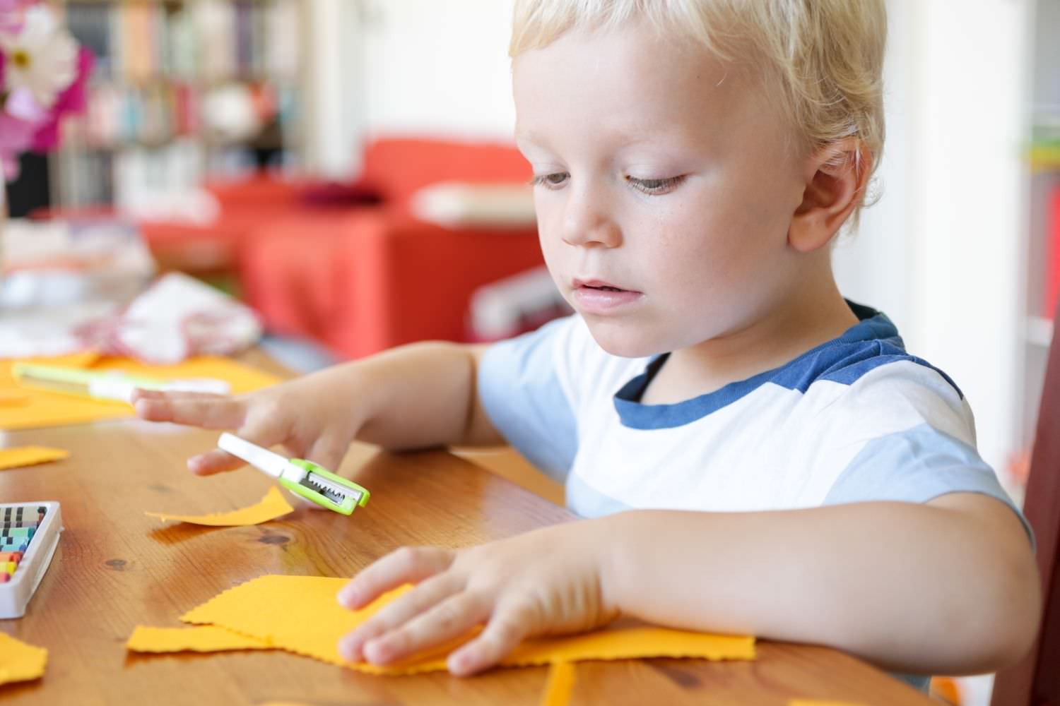 Bild zeigt: Kleiner Junge sitzt am Tisch und schneidet Papier
