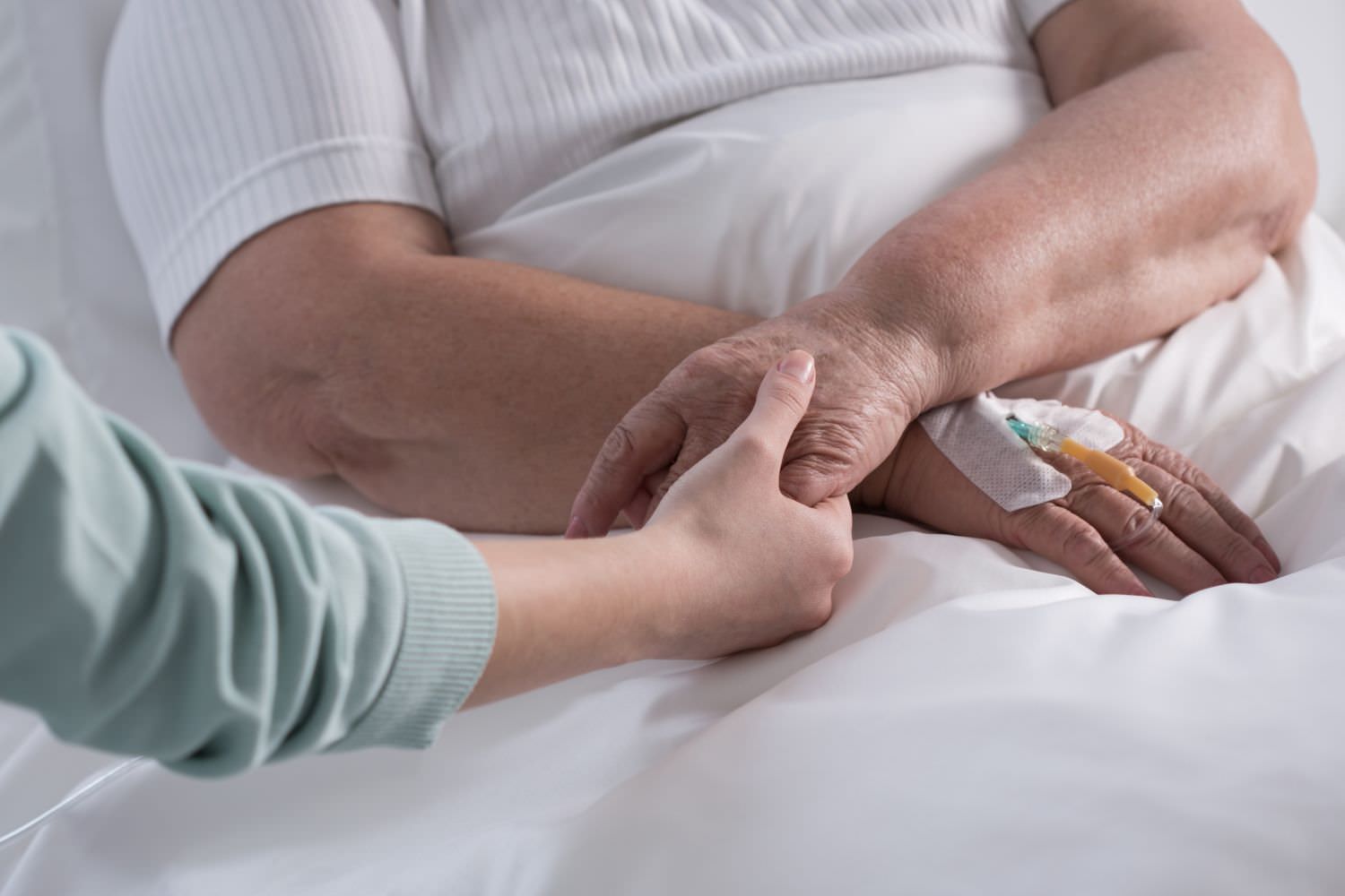Bild zeigt: Junge Frau hält die Hand einer kranken Frau im Krankenahaus