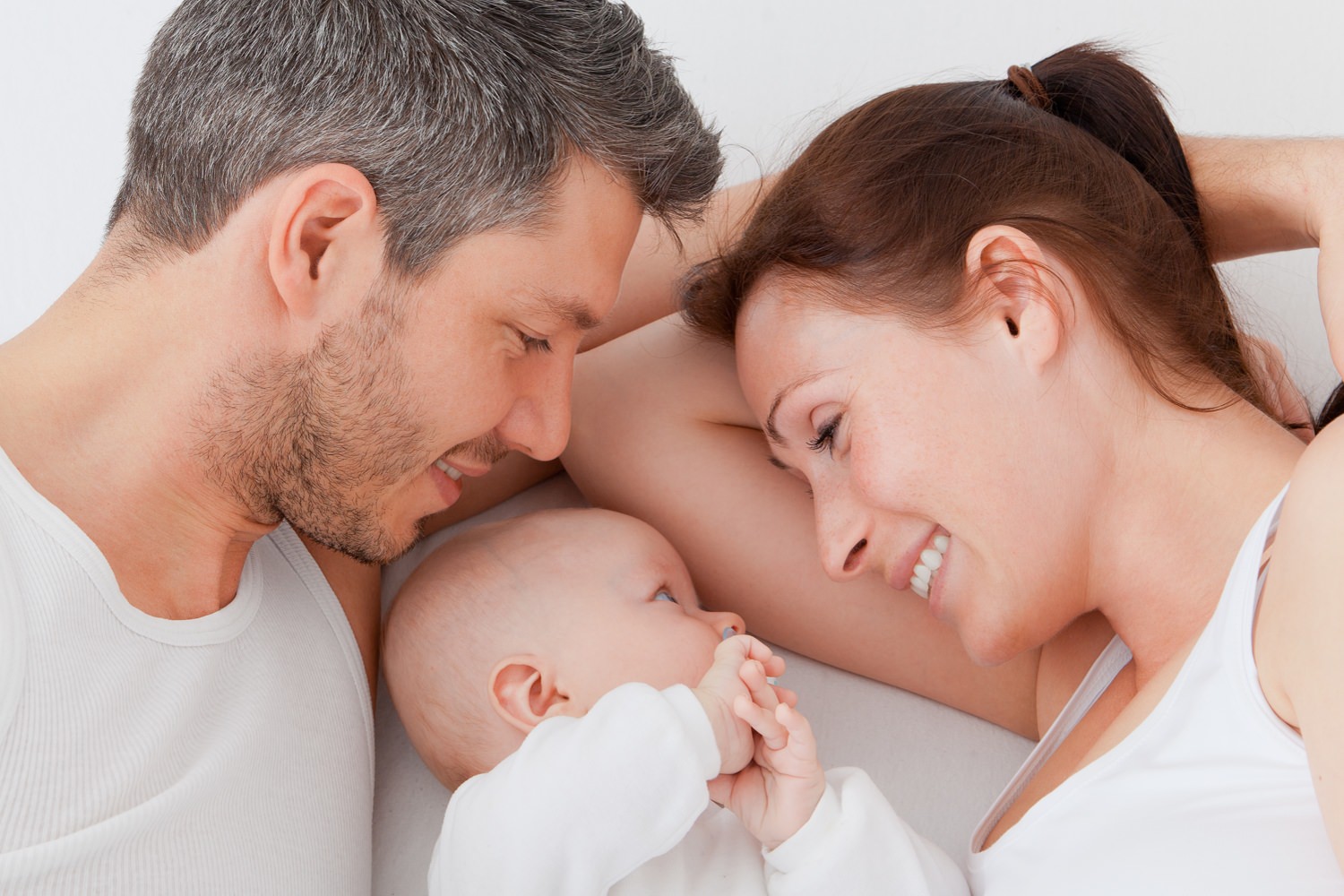 Bild zeigt: Säugling liegt zwischen jungen Eltern auf dem Bett