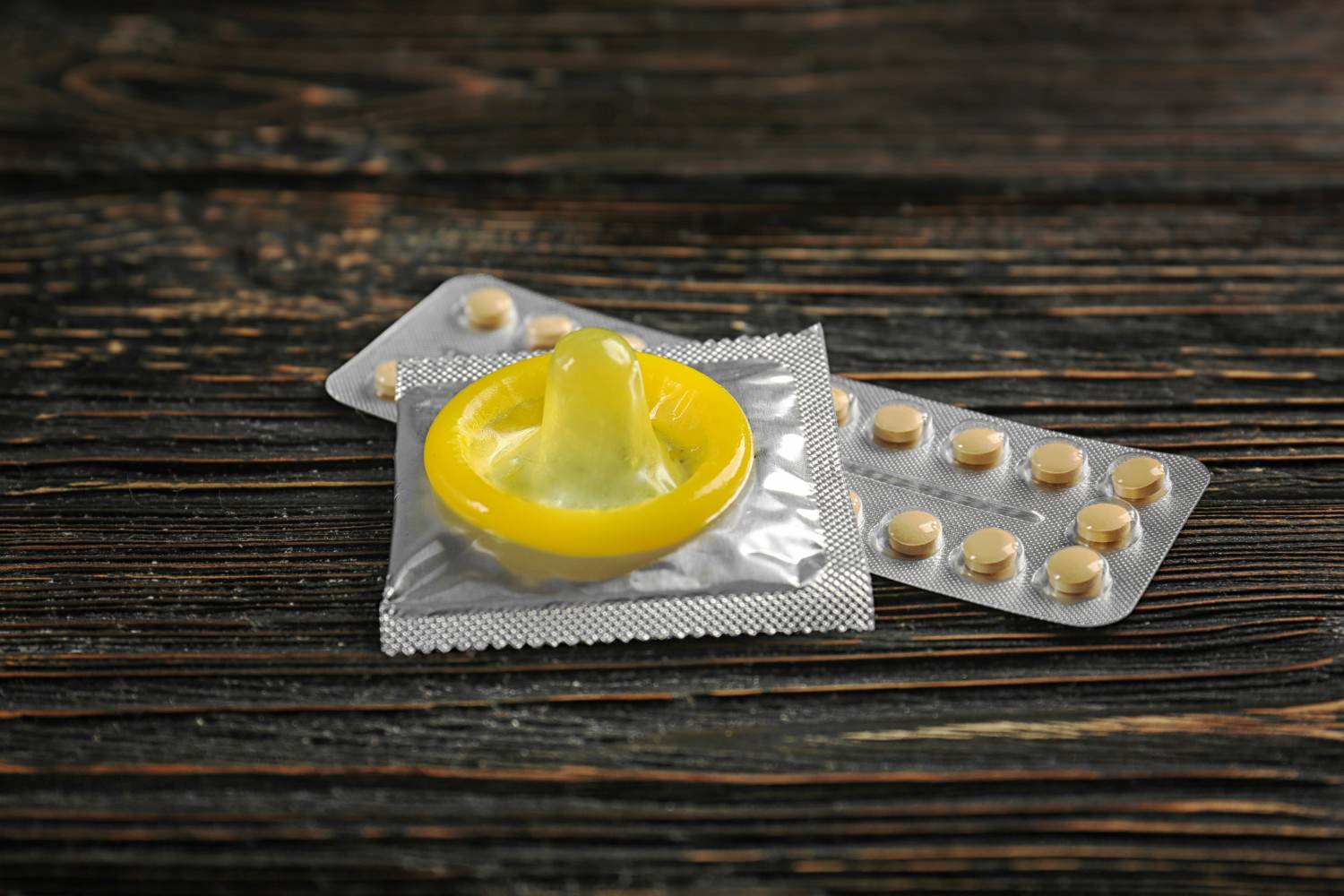 Bild zeigt: Gelbes Kondom und Pillenblister auf einem Holztisch