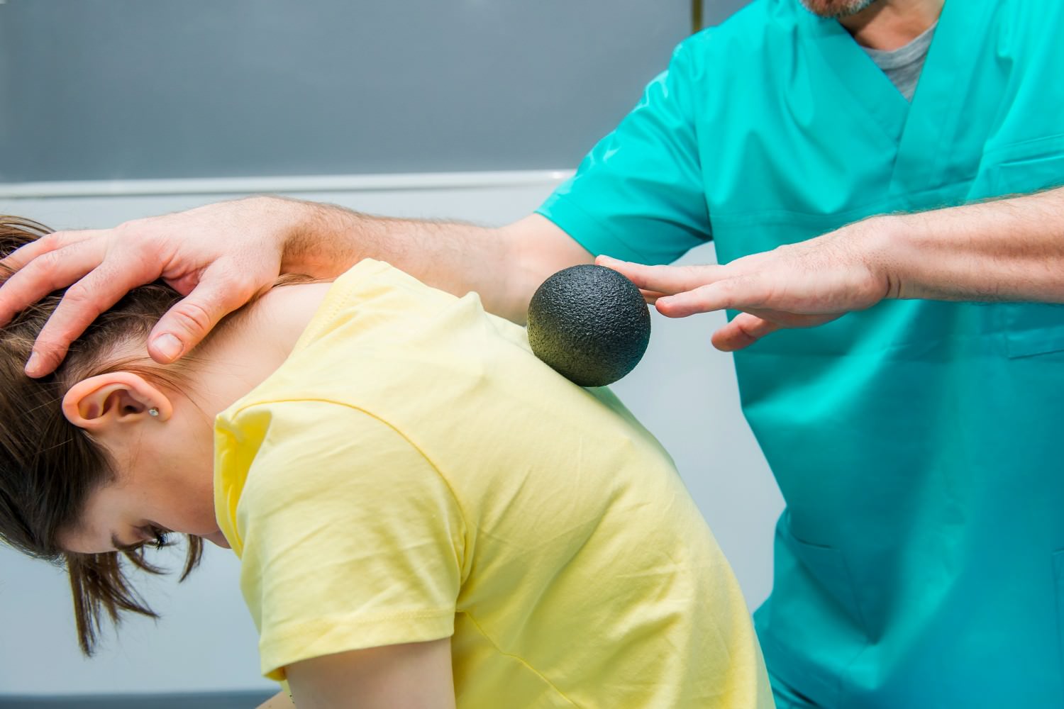 Bild zeigt: Physiotherapeut rollt mit einem Ball über den Rücken der Patientin
