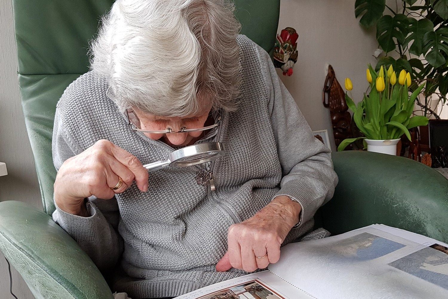 Bild zeigt: Eine alte Frau schaut mit Lupe in ein Fotoalbum