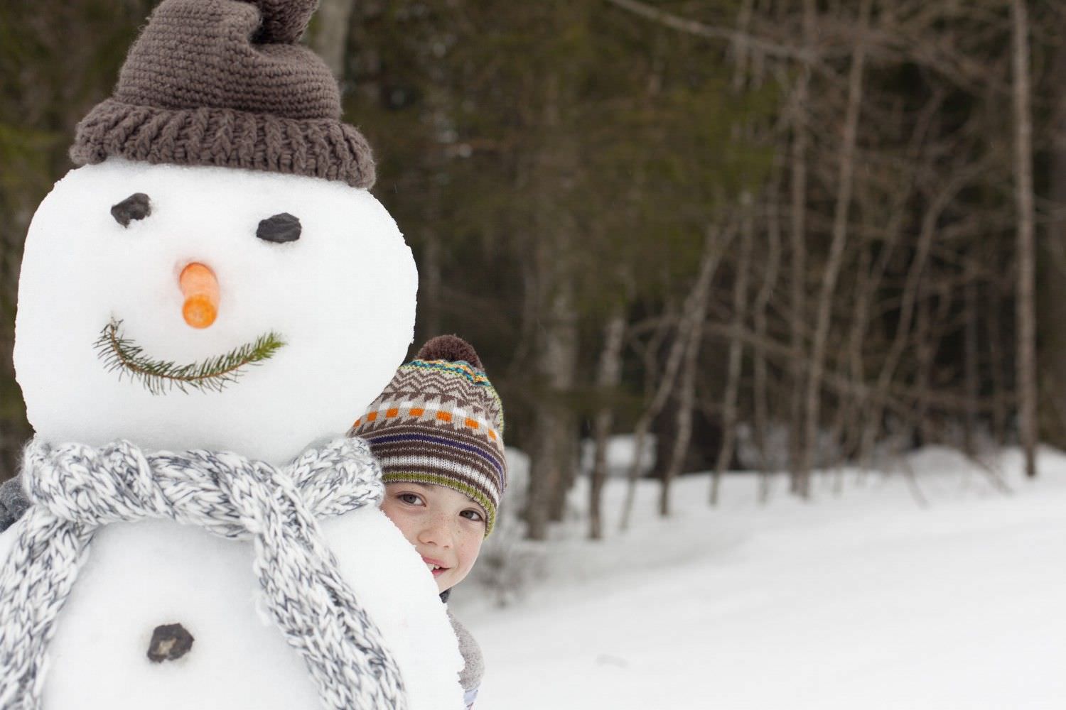 Bild zeigt: Kleines Mädchen versteckt sich hinter einem Schneemann