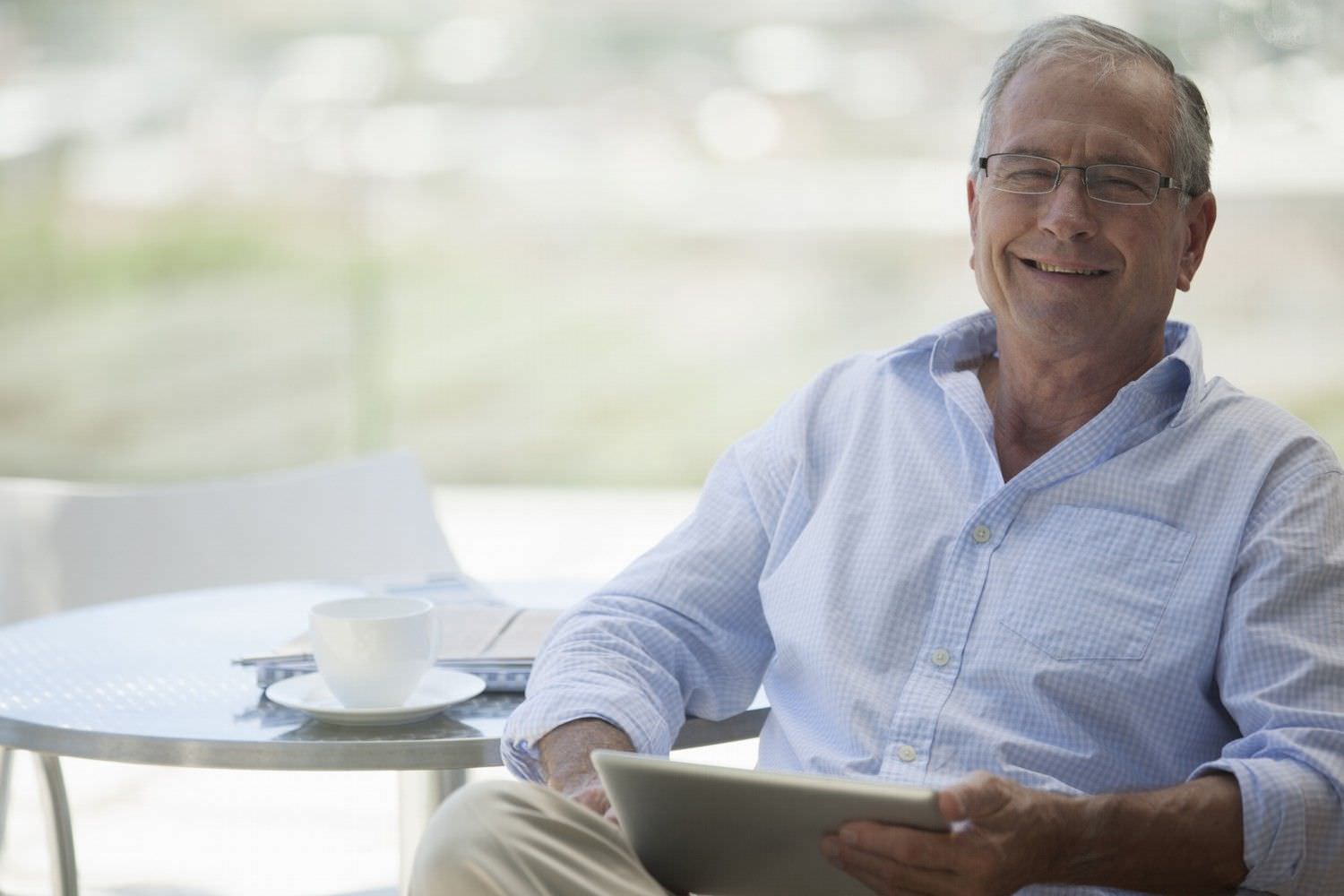 Bild zeigt: Älterer Mann draußen im Cafe mit Laptop lächelt