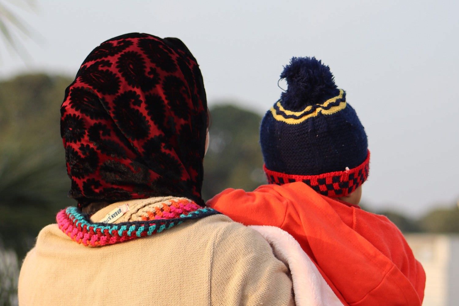 Bild zeigt: Von hinten Frau mit Kopftuch und Baby auf dem Arm