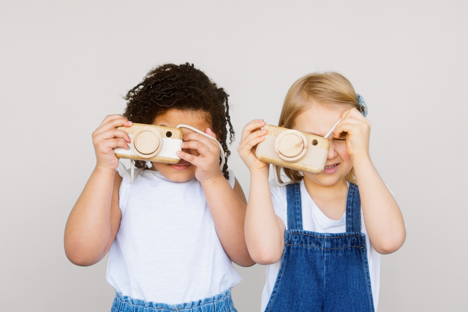 Bild zeigt: Zwei kleine Mädchen halten sich einen Fotoapparat aus Holz vor das Gesicht