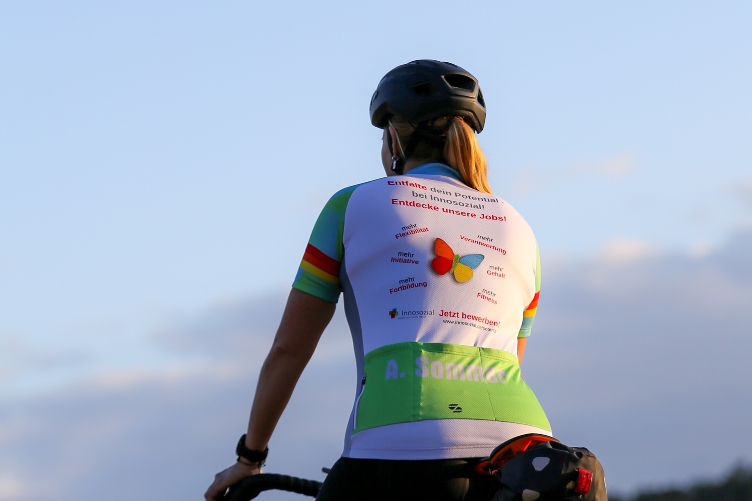 Bild zeigt: Eine Radfahrerin mit Helm von hinten und ihrem bedruckten Trikot