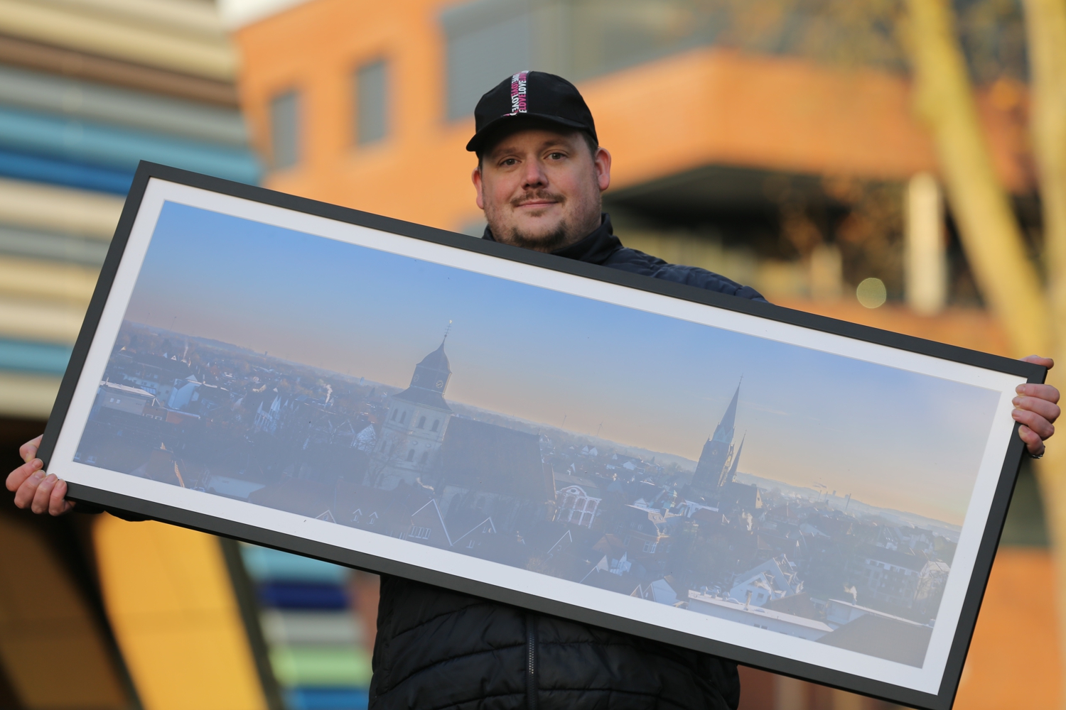 Bild zeigt: Fotograf Timo Junker hält einen Bilderrahmen mit Foto von Ahlen vor seinem Oberkörper