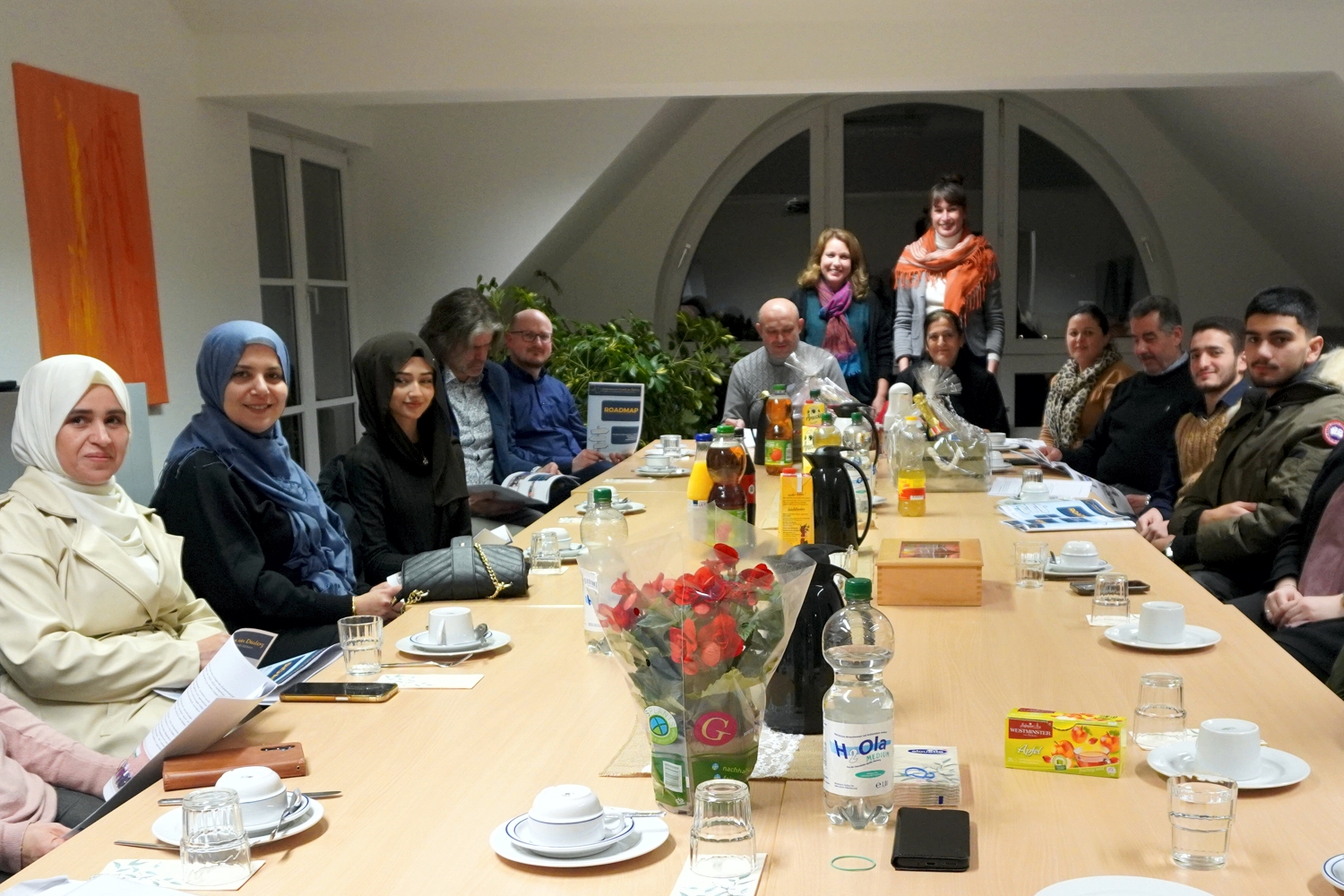 Bild zeigt: Interkulturelle Frauen und Männer sitzen in der Runde an großem Tisch